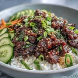 Overhead shot of an Easy Korean Beef Bowl with tender meat in a glossy red sauce, nestled on white rice and topped with fresh green onions, sesame seeds, and sliced radish.
