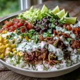 Golden brown carnitas burrito bowl with fluffy rice, black beans, corn, and zesty lime crema drizzle.