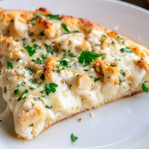 Sliced Chicken Alfredo Pizza on a wooden board, showing the crisp crust and red onion garnish, ready for a family dinner.  