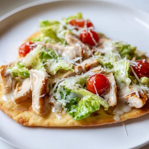 A close-up of Caesar Chicken Flatbread drizzled with creamy dressing and topped with shaved Parmesan and halved cherry tomatoes.