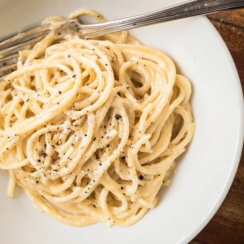 Spaghetti Cacio e Pepe is twirled onto a fork, showcasing its simple, luxurious Roman-inspired flavors for a comforting meal.  
