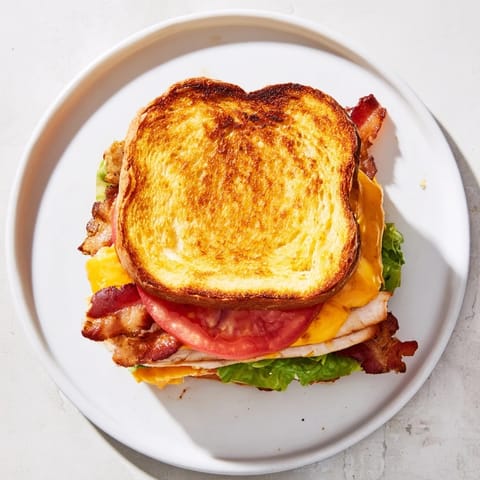 A close-up view of a sliced Turkey Club Grilled Cheese reveals layers of juicy turkey, bacon, and melted cheese on a plate.