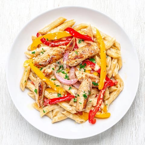 A skillet of Creamy Cajun Chicken Pasta Lite shows colorful bell peppers and onions mixed into a velvety, lighter Cajun cream sauce.  