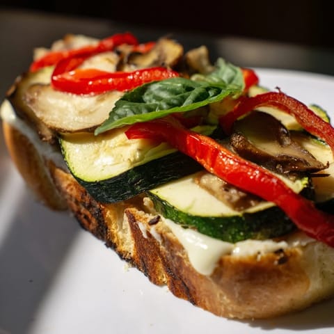 The roasted veggie Caprese grilled cheese rests on a plate, golden sourdough slices oozing melted mozzarella and vibrant roasted peppers and zucchini.