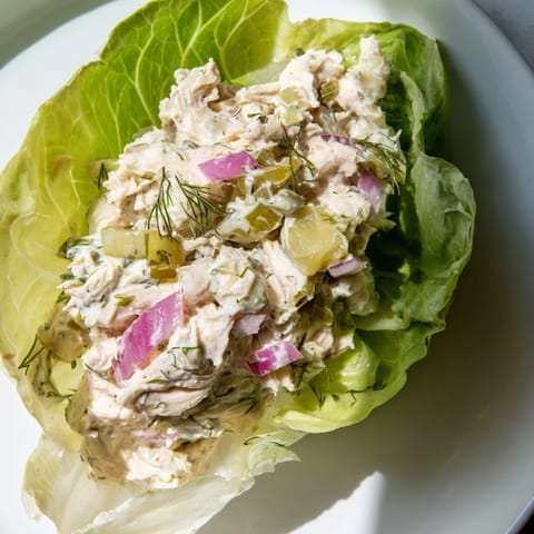 Fresh dill pickle chicken salad filling crisp, green butter lettuce cups on a white plate.