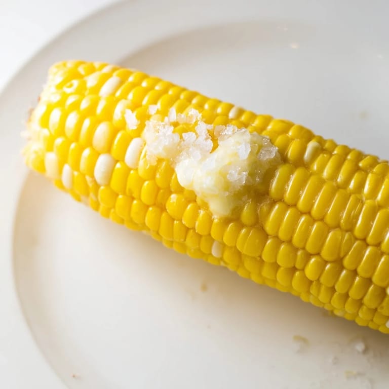 Close-up shot: Buttered corn on the cob, showing juicy kernels and perfect grill marks.