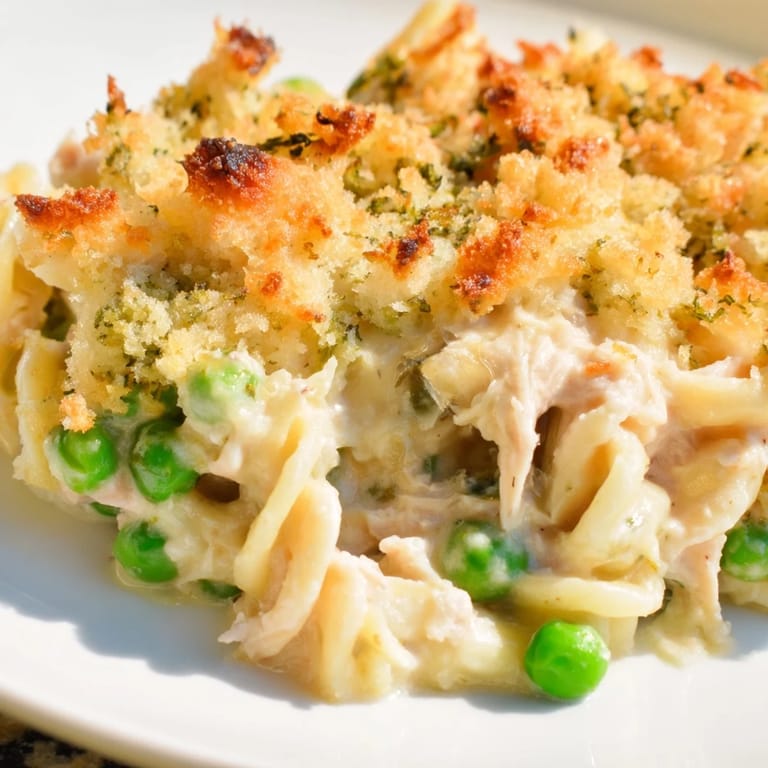 A close up shows bubbly Tuna Casserole, with visible pieces of tuna mixed into a creamy sauce under a golden crust.