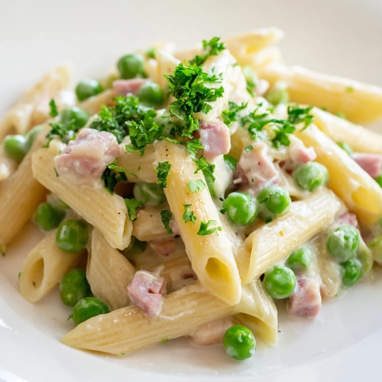 A serving of Spring Pea & Ham Pasta garnished with parsley and parmesan, ready to eat.
