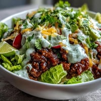 A vibrant Healthy Taco Bowl with seasoned ground beef, crisp romaine, and fresh tomatoes topped with zesty lime yogurt crema.